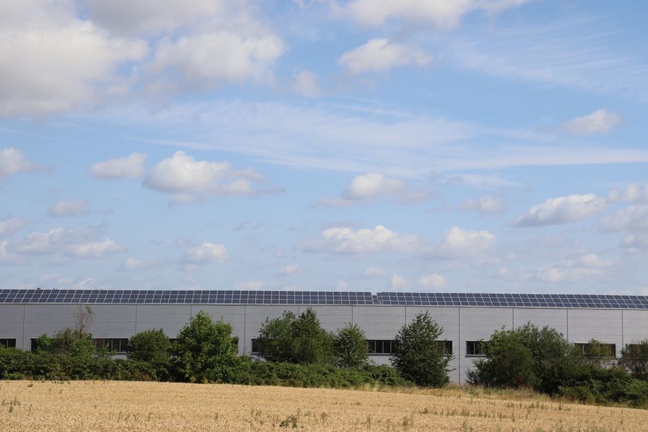 Energia Renovável — A countryside warehouse with solar panels and fields under a blue sky with clouds.